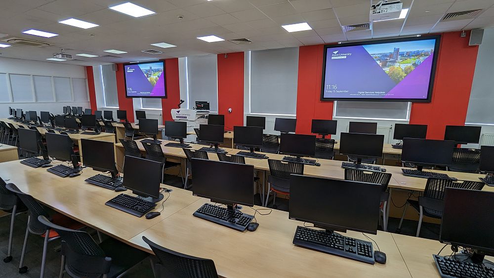 Modern computer lab with rows of workstations at Aston university.